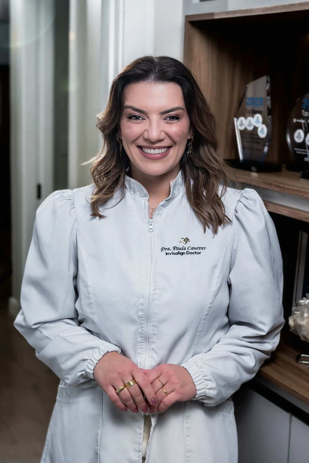 Dra. Paula Canever no consultório, com os reconhecimentos Invisalign ao fundo